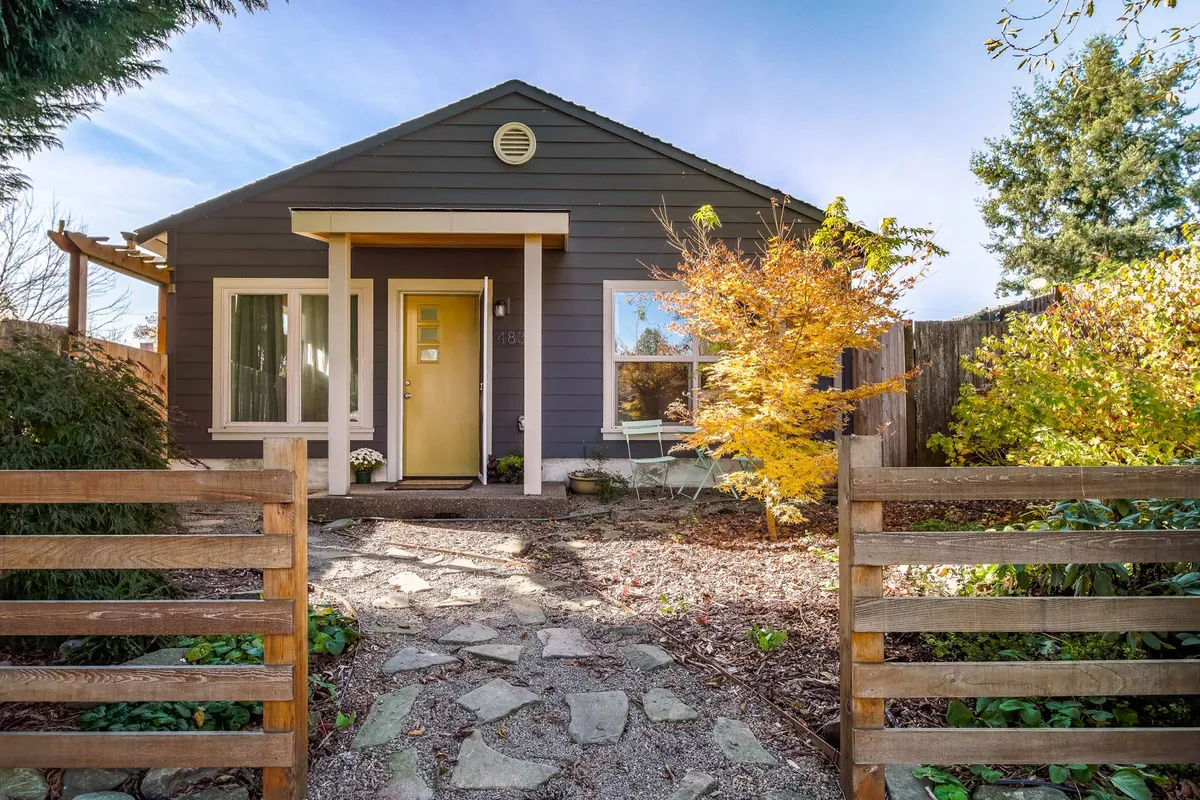 The image showcases the inviting exterior of a single-family guesthouse nestled under golden autumn foliage, with a charming stone pathway leading to a welcoming front door. The yellow tree provides a stunning seasonal backdrop, while the porch hints at a peaceful spot for morning coffee or relaxing outdoors.