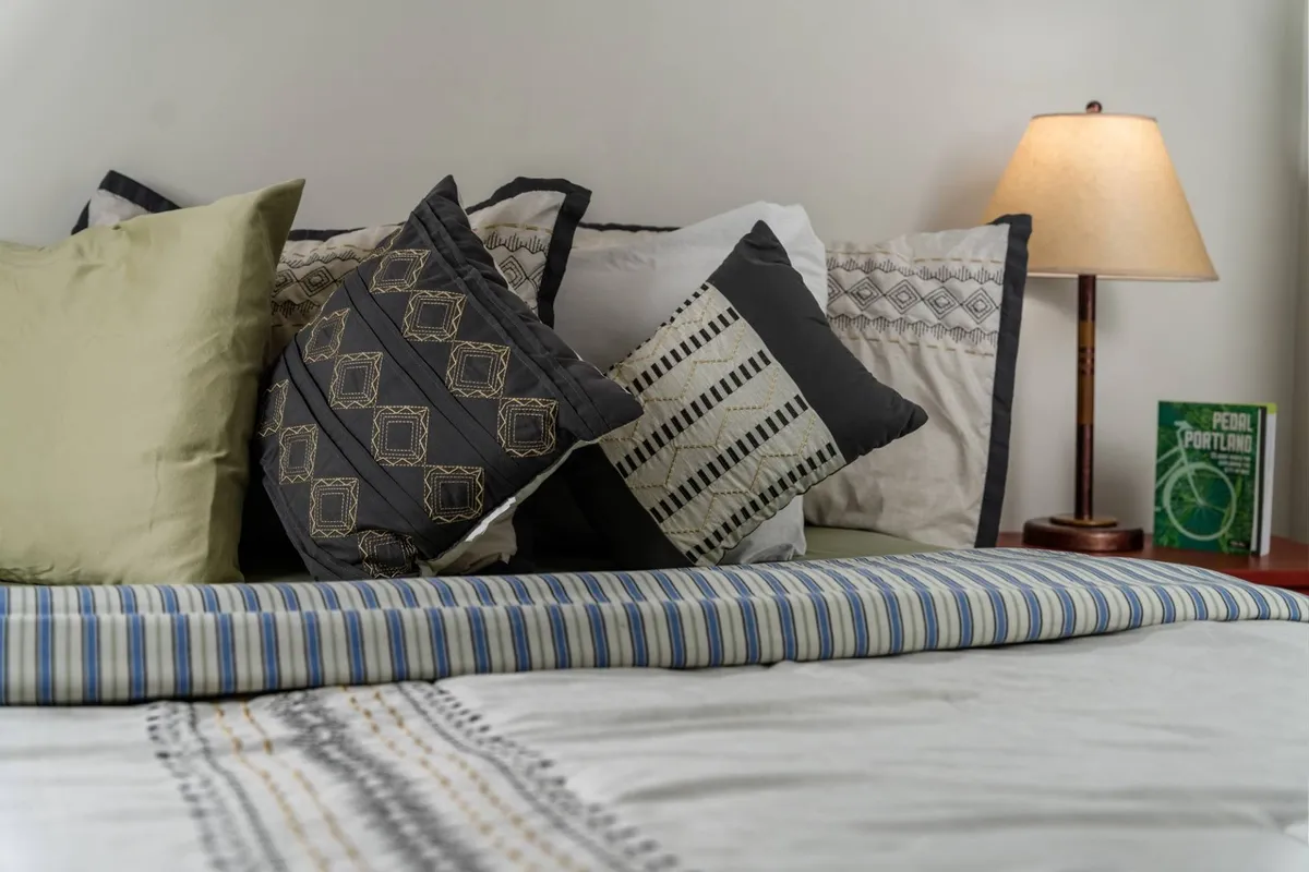 A cozy corner of the bedroom showcasing a comfortable bed with an inviting bedspread, decorative pillows, a bedside lamp, and a book, suggesting a space perfect for relaxation and quiet reflection.
