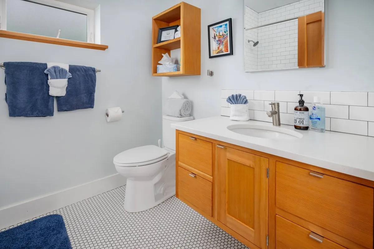 A bright, modern bathroom featuring a vanity with sink, fresh towels, a clean shower area, and an organized layout, exuding a sense of privacy and tranquility.