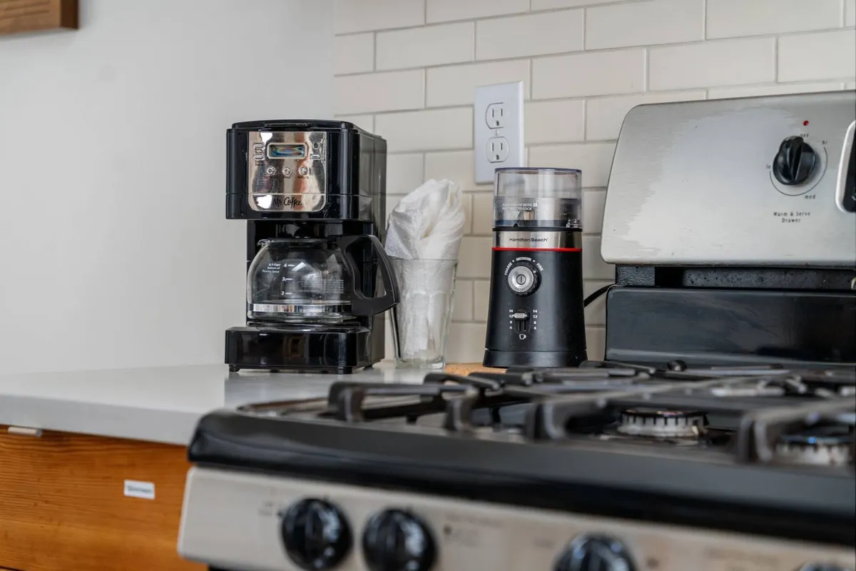 A welcoming kitchen scene featuring a coffee maker, grinder, and a stainless steel stove. The countertop is uncluttered, highlighting ample prep space, and the setup suggests a well-appointed area perfect for brewing morning coffee and preparing breakfast.