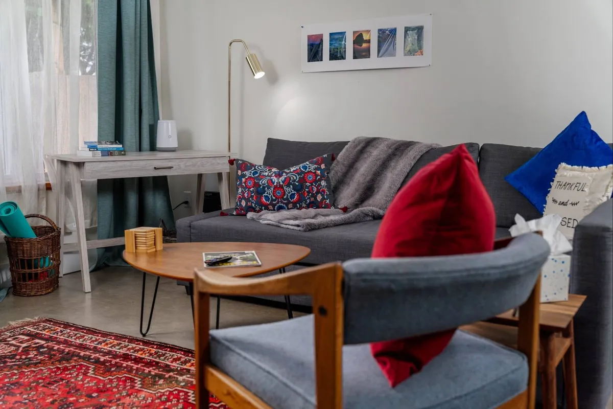 A modern living space with a plush sofa, coffee table, decorative pillows, and statement artwork. Soft, inviting tones and ample light create a welcoming nook, perfect for reading, relaxing, or socializing with friends and family.